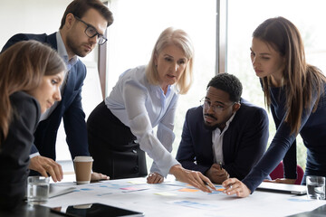 Aged leader young teammates discuss financial report at meeting, serious focused workers involved...