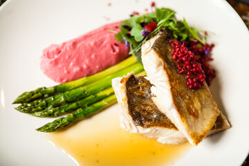 Pike-perch fillet. Asparagus, pearl couscous, white wine sauce, beet-flavored mashed potatoes. Delicious seafood fish closeup served on a table for lunch in modern cuisine gourmet restaurant