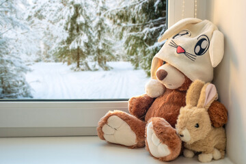 Best friends teddy bear and bunny toy sitting on window sill hugging each other and looking out of...