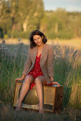 Atmospheric portrait of a young woman in a red dress sitting on an old retro TV in nature. The...