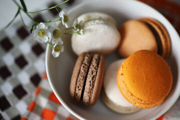 Cakes macaroons in a white bowl on a checkered napkin decorated with a white flower