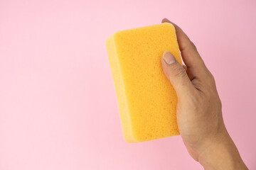 Hand holding a sponge isolated on pink background.