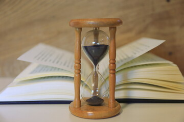 A close up of an hourglass on the table Open book in the background