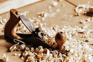 A black   jack plane is on a wooden table, next to a wooden sawdust in the workshop