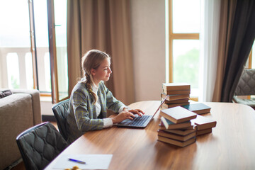 Young smiling teen schoolgirl student sitting with books and working at laptop. Back to school. Exam preparation
