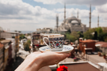 Traditional Turkish tea cup with ornaments in hands with the view of mosque in Istanbul