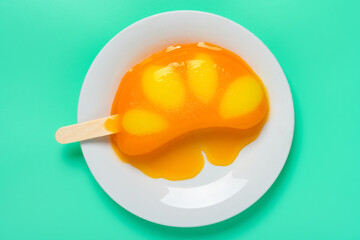 top view orange shape and flavor popsicle starts melting on a plate