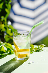 glass with refreshing drink with ice, lemon and straws, on a green background and umbrella. Summer drink.