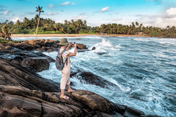 girl in a hat takes pictures of the ocean by smartphone