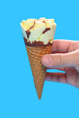 hand holding a fresh vanilla flavor ice cream cone on blue background