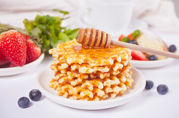 Plate with sweet tasty waffles with honey, berries, cup of tea on the white background.
