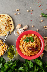 Hummus topped with chickpeas, sun dried tomatoes and green coriander leaves on stone table with pita bread aside