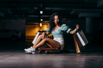 Beautiful afro american  sitting on a skateboard with shopping bags in the underground Parking