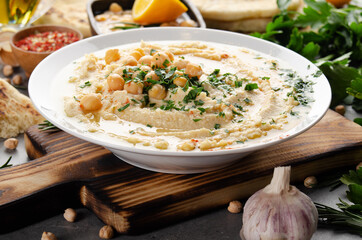 Fresh homemade Hummus in clay dish topped with olive oil, chickpeas and chopped green coriander leaves on stone table served with spices