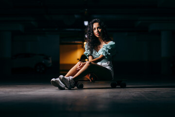 Obraz na płótnie Canvas Beautiful afro american girl sitting on a skateboard in the underground Parking