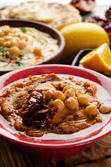 Fresh homemade Hummus in clay dish topped with olive oil, chickpeas, spices and sun dried tomatoes on stone table