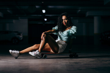 Beautiful afro american  girl sitting on a skateboard in the underground Parking