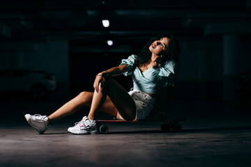 Beautiful afro american  girl sitting on a skateboard in the underground Parking