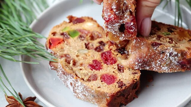 Piece of Christmas fruit cake on a plate in festive decorations, top view, dark background.