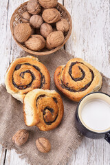 Basket of homemade buns with jam, served on old wooden table with walnuts and cup of milk