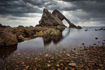 Bow Fiddle Rock on the Moray Coast, Scotland. Dreamy seascape water with leading line of small rocks to the main Big rock.