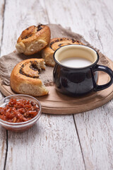 Variety of homemade puff pastry buns cinnamon served with milk cup, jam, butter as breakfast over white plank wooden background. Flat lay, space