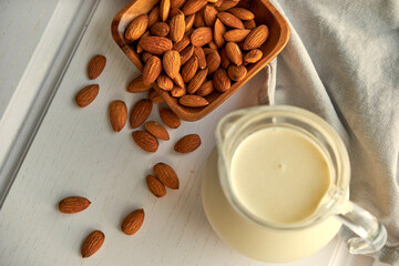 Almond milk in glass with almonds in wooden bowl on a white wooden table