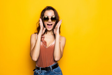 Young woman sunglasses looking away with surprised smile isolated on yellow background.
