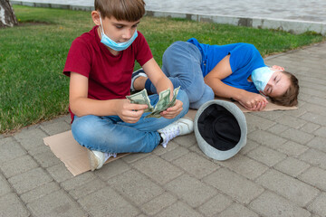 Naklejka premium The boy counts the money begged from passers-by on the street. His brother is sleeping next to him on a piece of cardboard.