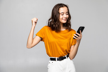 Naklejka premium Portrait of a satisfied young woman holding mobile phone and celebrating isolated over gray background
