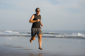 Fototapeta na wymiar outdoors running workout - young attractive and athletic runner man jogging on beautiful beach in Summer training happy and free in fitness and healthy lifestyle concept