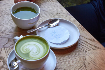 Cup of matcha latte and cup of matcha on the table in cafe 