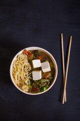 Japanese soup with vegetables, pasta, tofu cheese, chopsticks on a black background. Flat lay. Copy spaes.