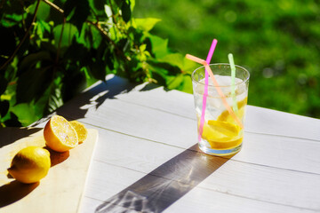 glass with refreshing drink with ice, lemon and straws, on a green background on a wooden surface....