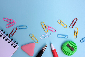 School stationery on a blue background. Back to school concept. Top view, copy space. Open paper notebook, red pen, eraser, green pencil sharpener and colorful paper clips.