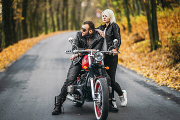 Fototapeta na wymiar Pretty couple near red motorcycle on the road in the forest with colorful blured background