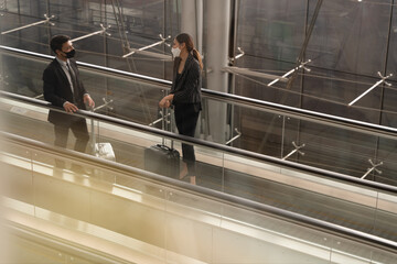 Two Businessman and woman having conversations while wearing face mask on escalator at the airport, New normal of people to stay safe and awareness for prevent coronavirus or covid-19 pandemic.