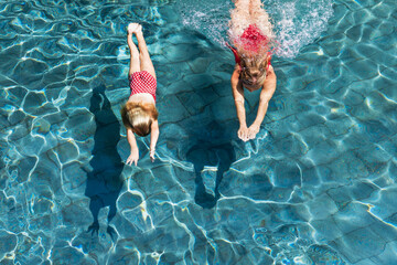 Happy family in swimming pool. Child with young woman swim, dive in pool with fun - jump deep down...