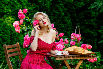 Beautiful blonde girl in red dress drinking a coffee in a garden