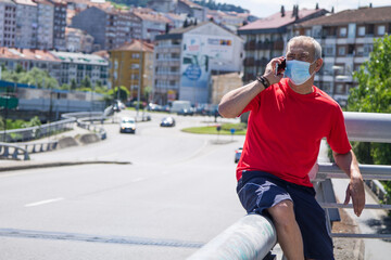 mature man with medical mask doing sports and using mobile phone in the city, concept of sport and technology in the new normal