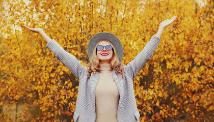 Autumn day, stylish young woman raising her hands up wearing gray coat, round hat over yellow leaves background