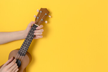 Female hands hold ukulele on a bright yellow background. Education the play on hawaiian guitar...