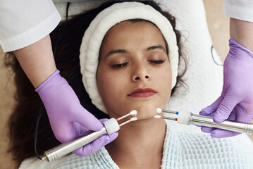 Young happy woman on modern cosmetic procedures. Skin care spa concept. Closeup Of Beautiful Woman Receiving Facial Microcurrent Treatment From Therapist At Spa Salon