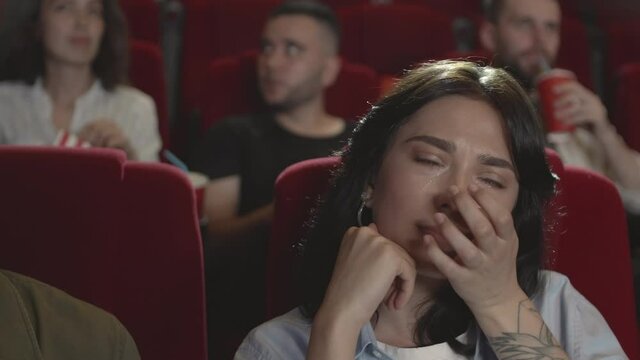 Close up of beautiful Caucasian woman is sitting in cinema and crying because of touching movie she is watching