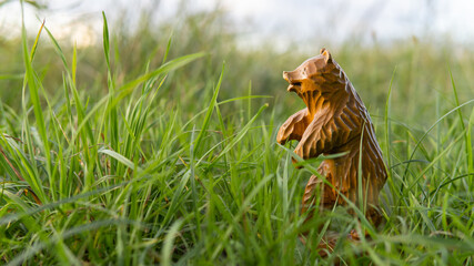 A small carved figure of a bear. Wood carving. A wooden bear sculpture stands in the green grass outside.	