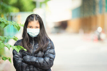 Asian Young Woman wearing black jacket and face medical masked. Standing and crossing her arms in public place, during covid19 virus pandemic. Protective equipment to help keep us safe new life.