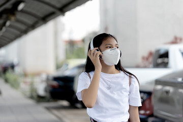 Asian young woman walking on street with her headphones while wearing face mask as protection against infectious diseases during coronavirus pandemic. Basic equipment to help keep us safe new life.