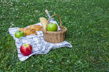 Romantic summer picnic lunch outdoors. Wicker basket with croissants, apples and bottle of rose...