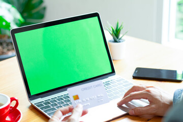 Business concept : Young man hands holding credit card and using laptop, online shopping and image blank screen computer with green background for advertising text.