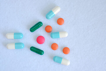 Pills tablets and capsules are scattered over a white background.